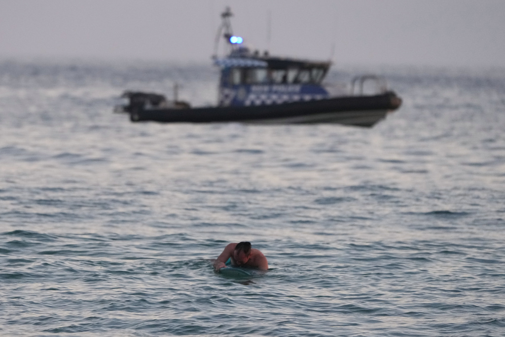 A surfer paddles back to shore as a police boat patrols the water after a reported shooting at Bondi Beach in Sydney, Sunday, Dec. 14, 2025. (AP Photo/Mark Baker)