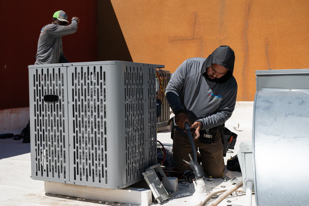 FILE - Sonel Telemaque, left, wipes sweat from his brow while installing a new air conditioning unit alongside Brian Hermosillo during record-breaking heat March 19, 2026, in Tempe, Ariz. (AP Photo/Caitlin O'Hara, File)