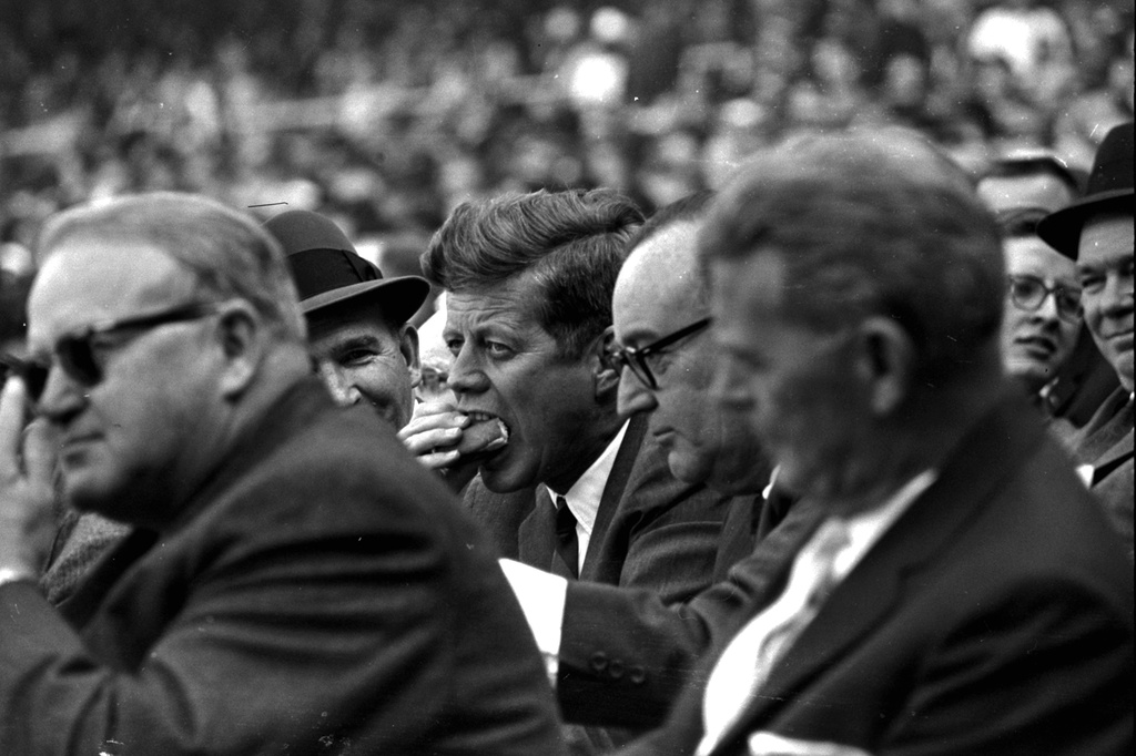 FILE - President Kennedy, with eyes glued on the playing field, munches a hot dog during the American League opener, April 8, 1963. The President stayed throughout the game, watching the Baltimore Orioles defeat the Washington Senators 3-1. (AP Photo/stf, File)
