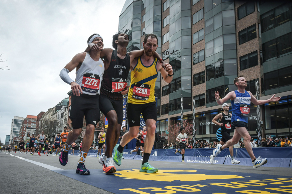 This photo provided by the Boston Athletic Association and Marathonfoto shows Boston Marathon runners Robson De Oliveira of Brazil, left, and Aaron Beggs, of Britain, right, helping runner Ajay Haridasse and helped him across the finish line Monday, April 20, 2026, in Boston. (Gustavo E. Gargallo/Boston Athletic Association/MarathonFoto via AP)