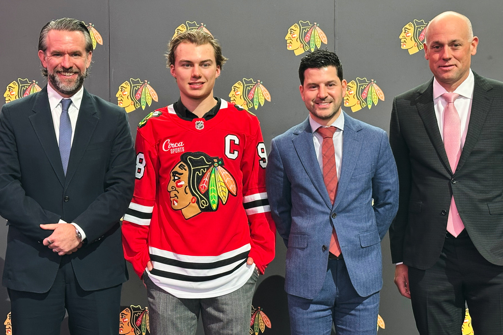 In this photo taken with a smartphone, Chicago Blackhawks Chairman Danny Wirtz, from left, player Connor Bedard, general manager Kyle Davidson and head coach Jeff Blashill pose during a news conference introducing Bedard as the new captain of the NHL hockey club, Tuesday, Sept. 15. 2026, in Chicago. (AP Photo/Jay Cohen)
