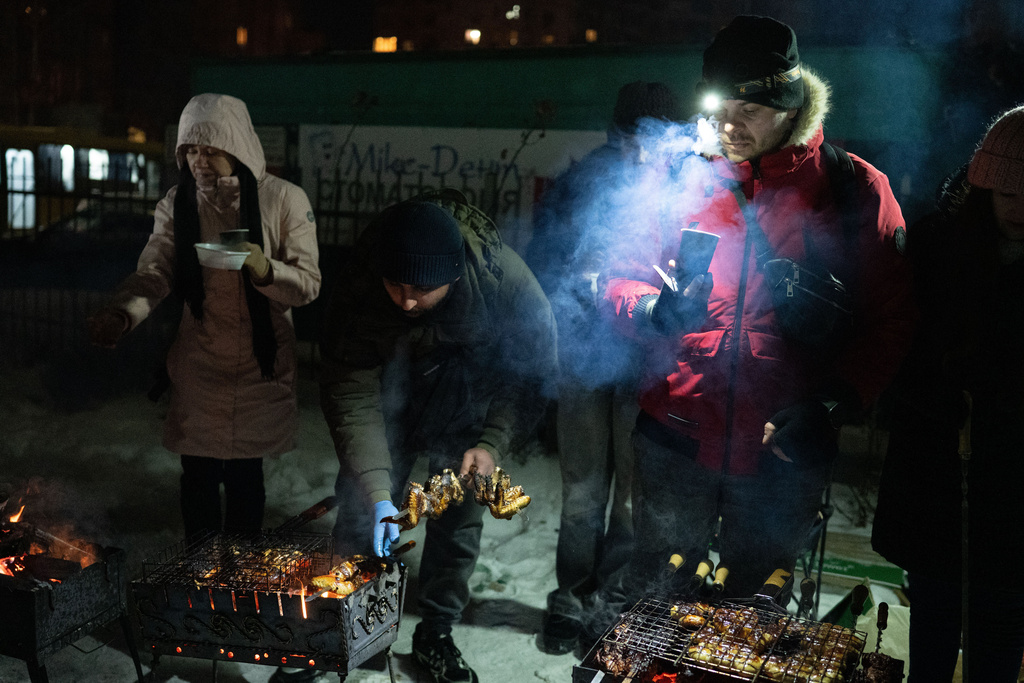 People cook on grills and warm up outside their multistory buildings during a power outage caused by Russia's regular air attacks on the country's energy sector that leave residents without power, heating and water in Kyiv, Ukraine, Sunday, Jan. 18, 2026. (AP Photo/Danylo Antoniuk)