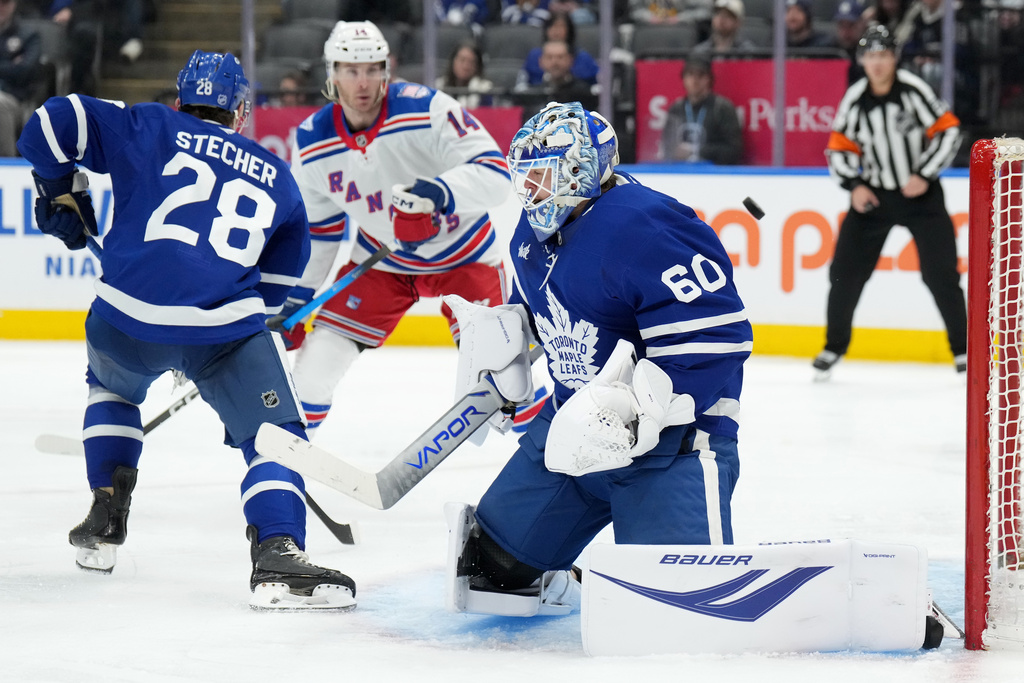 Toronto Maple Leafs goaltender Joseph Woll (60) makes a save as teammate Troy Stecher (28) and New York Rangers forward Taylor Raddysh (14) look on during the third period of an NHL hockey game in Toronto, Wednesday, March 25, 2026. (Nathan Denette/The Canadian Press via AP)
