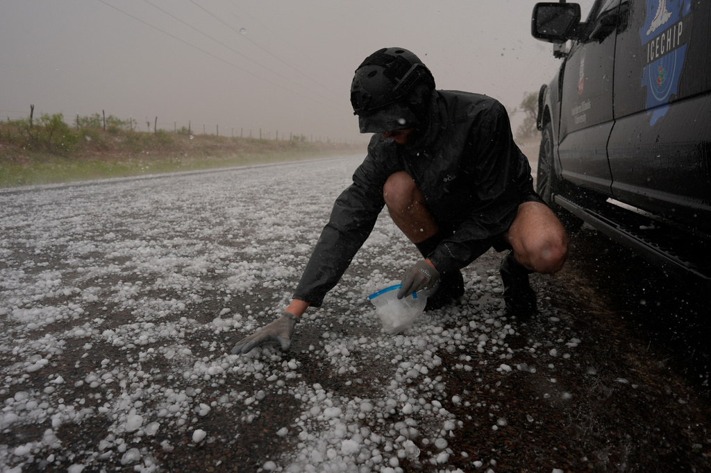 FILE - Tony Illenden crouches in a helmet and gloves outside Northern Illinois University's Husky Hail Hunter vehicle to scoop hail into a bag during a storm while on a Project ICECHIP operation June 6, 2025, in Levelland, Texas. (AP Photo/Carolyn Kaster, File)