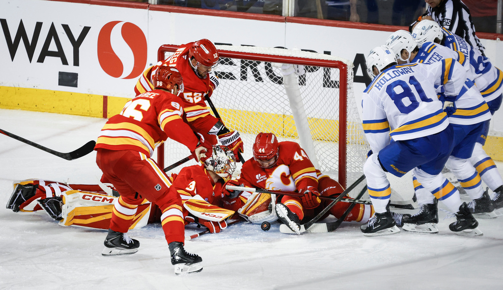 St. Louis Blues, left to right, Dylan Holloway, Pius Suter, and Jake Neighbours, try to get at a loose puck as Calgary Flames, left to right, Joel Farabee, MacKenzie Weegar, goalie Dustin Wolf, and Joel Hanley pile into the net during the third period of an NHL hockey game in Calgary, Alberta, Saturday, Oct. 11, 2025. (Jeff McIntosh/The Canadian Press via AP)
