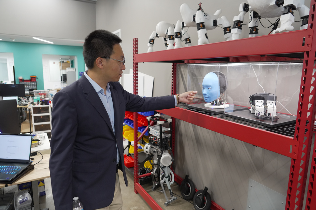 Professor Boyuan Chen gestures toward a humanoid robot at Duke University's General Robotics Lab in Durham, N.C., Tuesday, May 26, 2026. (AP Photo/Allen G. Breed)