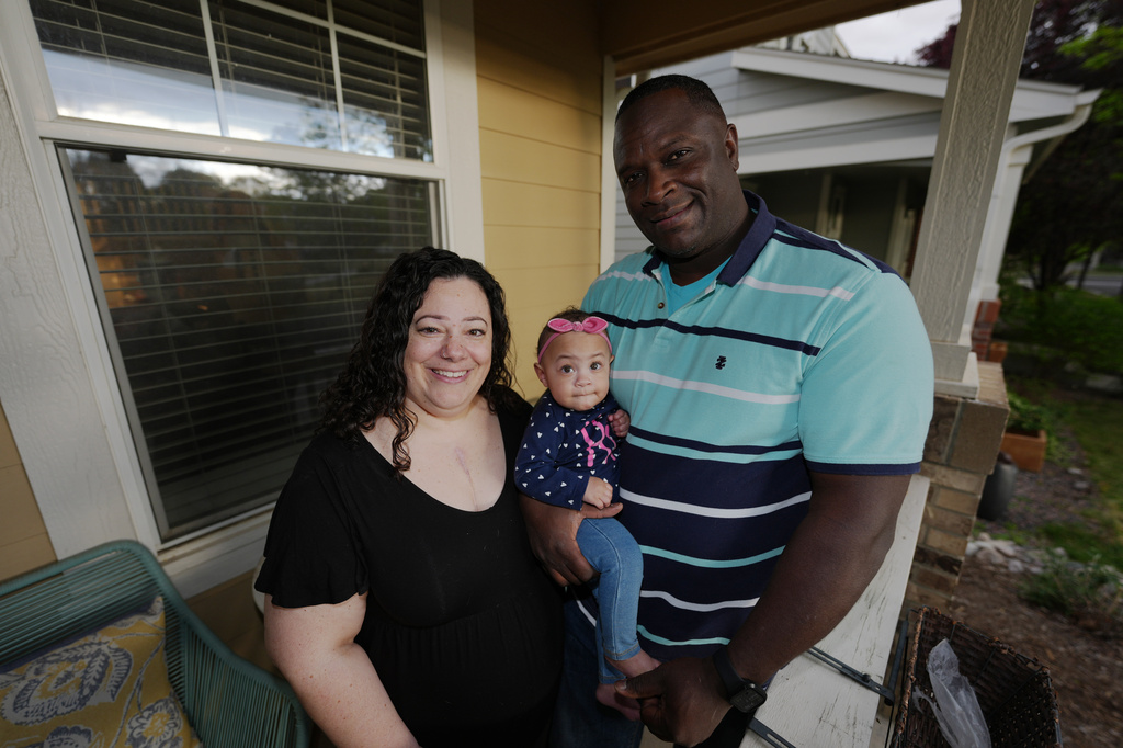 Farra White poses with her 1-year-old daughter, Olivia, and husband Marlon White outside their residence Thursday, May 7, 2026, in Fort Collins, Colo. (AP Photo/David Zalubowski)