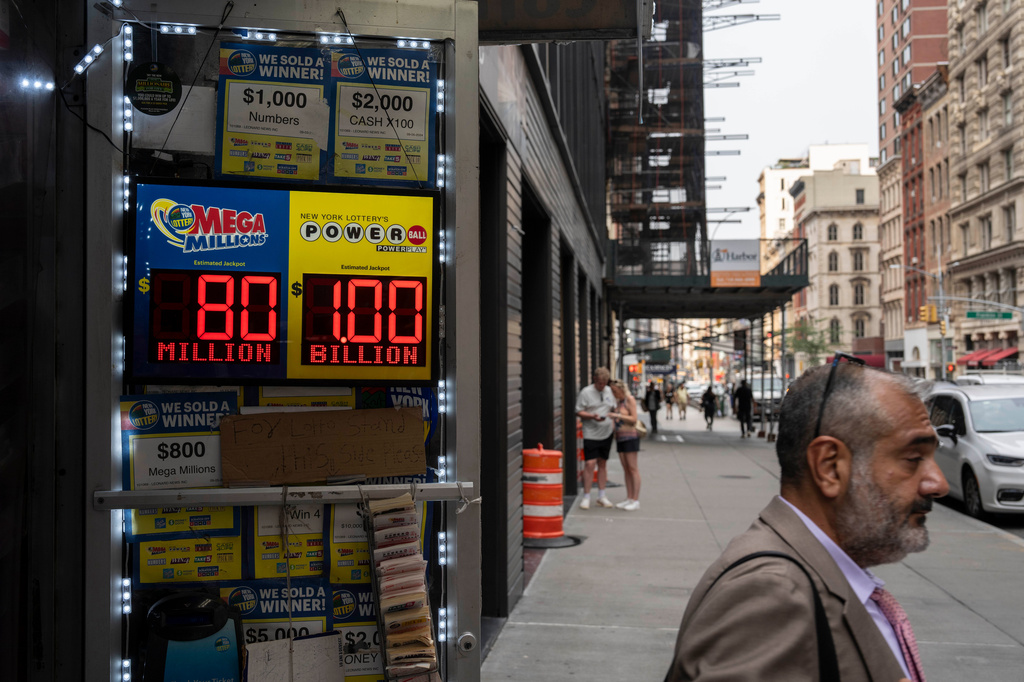 A person walks past a sign displaying the jackpot payout for Powerball outside a convenience store, Tuesday, Aug. 11, 2026, in New York. (AP Photo/Yuki Iwamura)