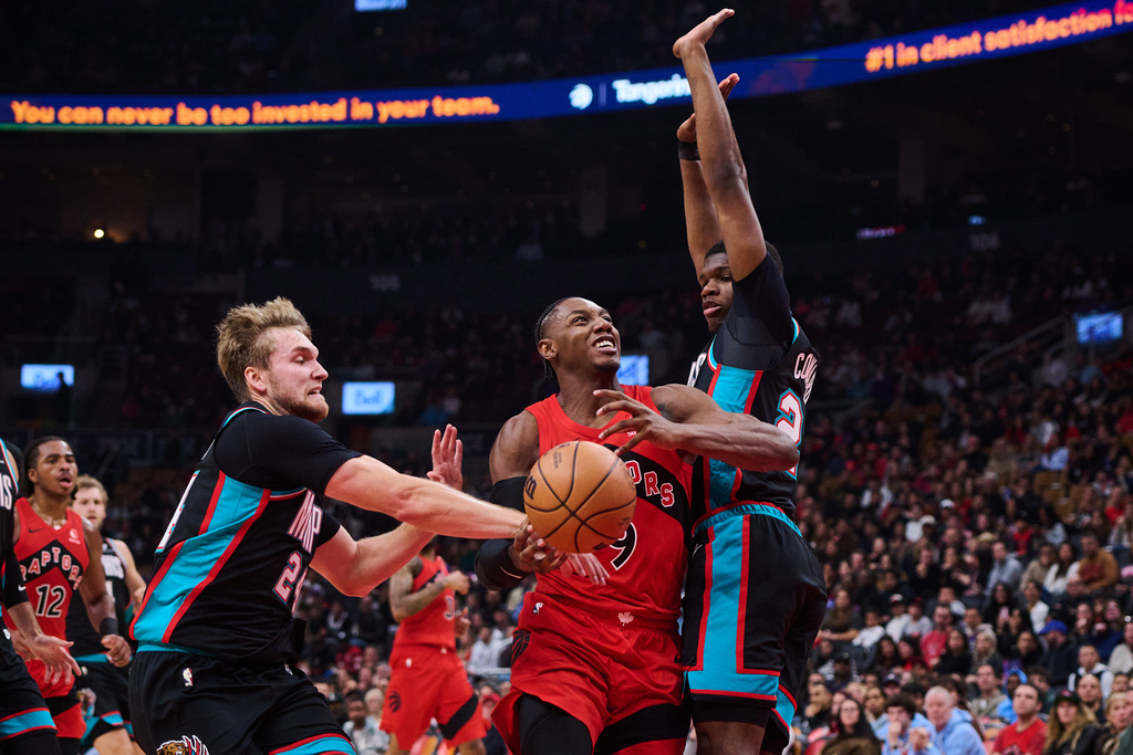 Toronto Raptors' RJ Barrett (9) drives between Memphis Grizzlies' Cam Spencer, front left, and Cedric Coward, right, during first-half NBA basketball game action in Toronto, Sunday, Nov. 2, 2025. (Sammy Kogan/The Canadian Press via AP)