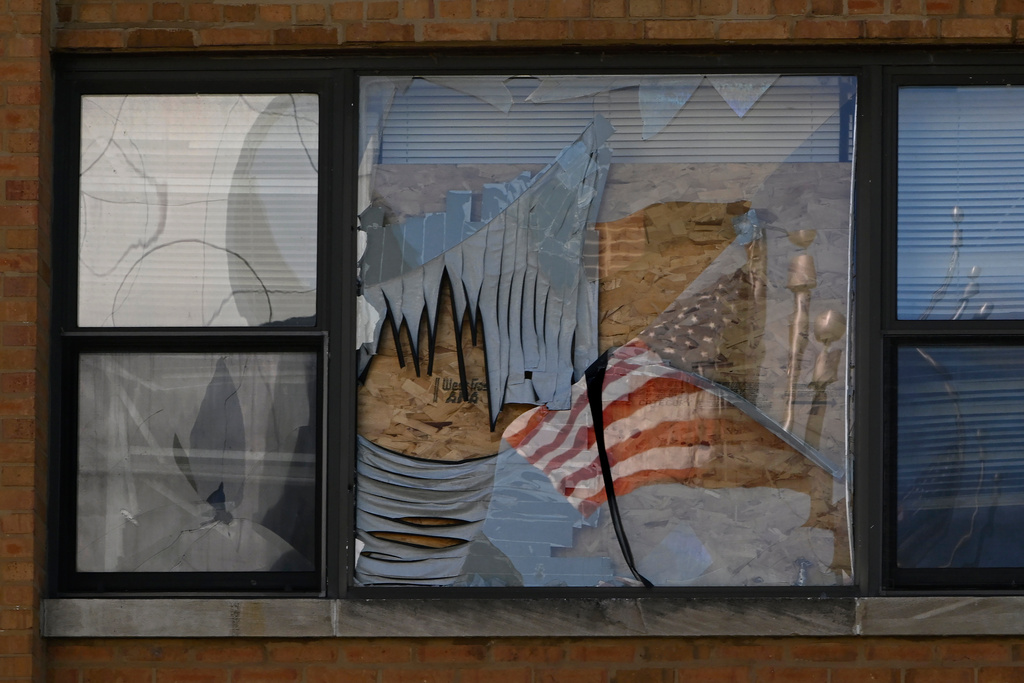 A U.S. flag is reflected in a broken window on Oct. 8, 2025, at the apartment building at 7500 South Shore Drive in Chicago, which was raided by ICE agents on Sept. 30. (AP Photo/Paul Beaty)