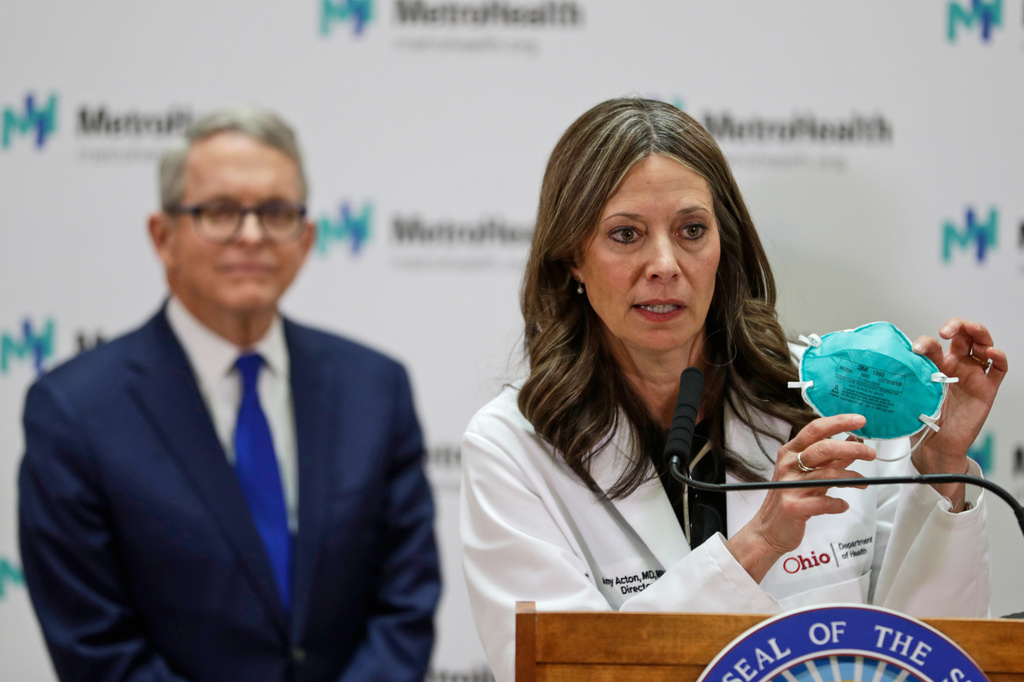 FILE - Ohio Department of Health Director Amy Acton holds up a mask as she gives an update at MetroHealth Medical Center as Ohio Gov. Mike DeWine, listens, Feb. 27, 2020, in Cleveland, on the state's preparedness and education efforts on COVID-19. (AP Photo/Tony Dejak, File)