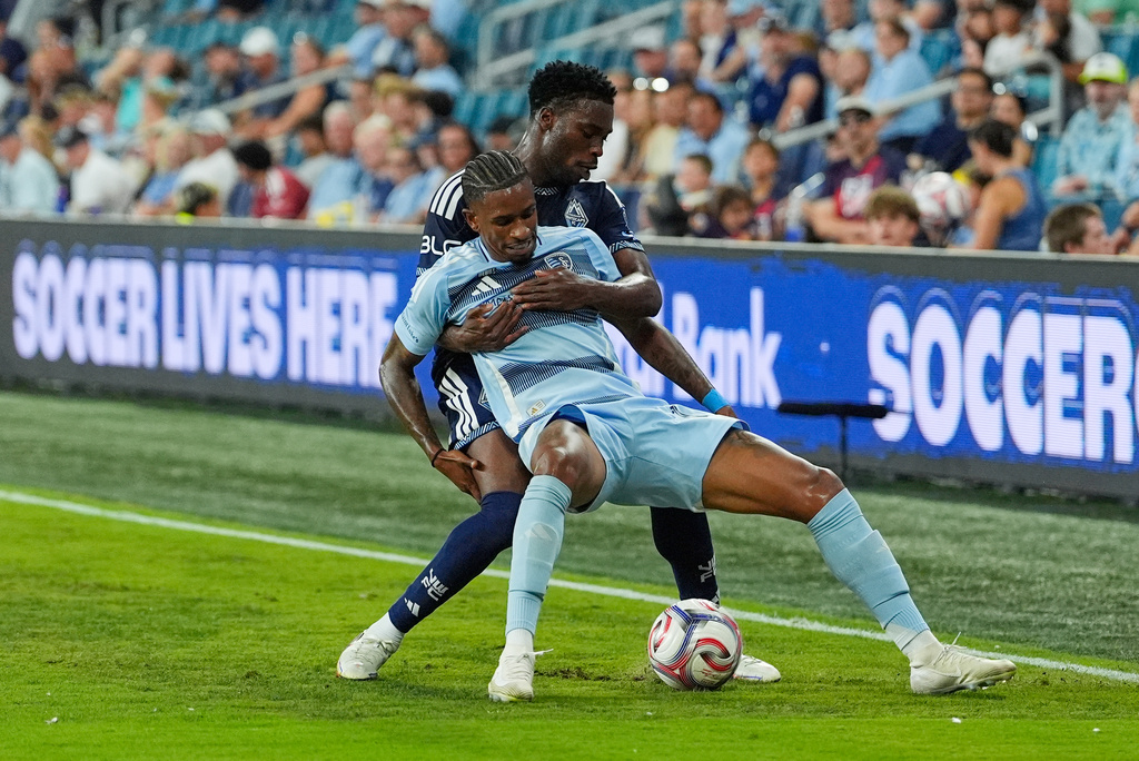Vancouver Whitecaps' Sam Adekugbe, back, battles for the ball with Sporting Kansas City's Andre Luiz during the second half of an MLS soccer match Saturday, Aug. 29, 2026, in Kansas City, Kan. (AP Photo/Charlie Riedel)