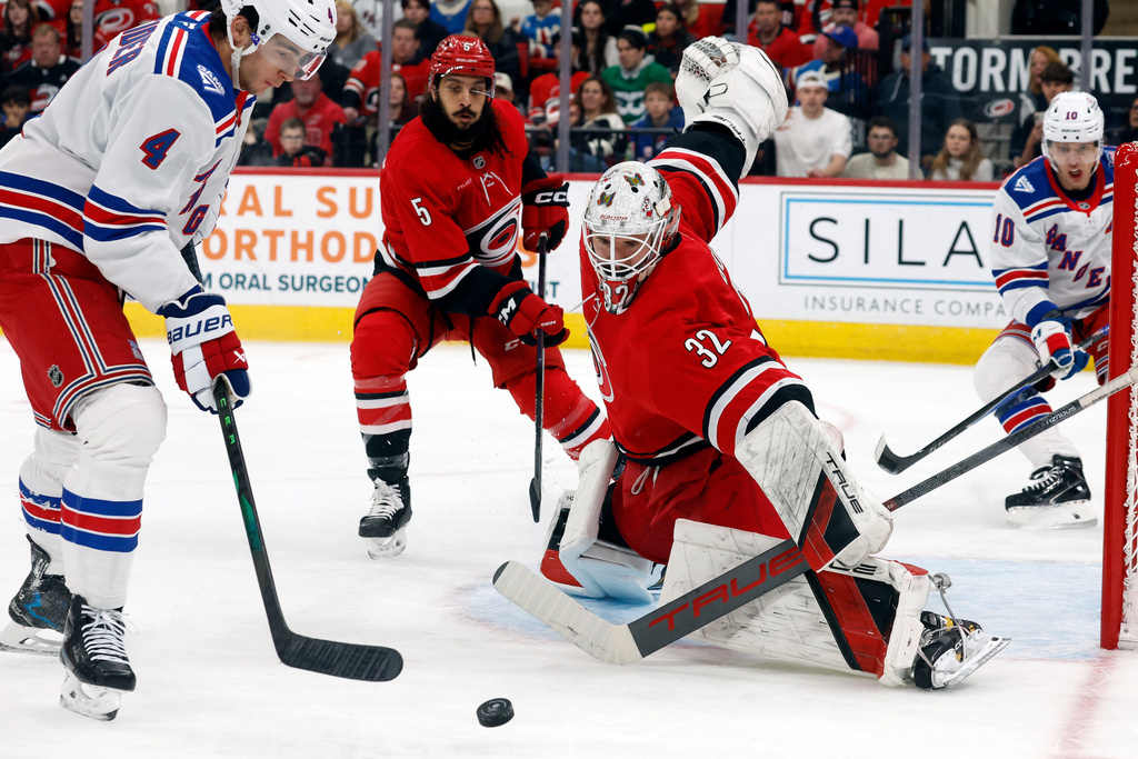 New York Rangers' Braden Schneider (4) tries to gather in the puck in front of Carolina Hurricanes goaltender Brandon Bussi (32) with Jalen Chatfield (5) nearby during the first period of an NHL hockey game in Raleigh, N.C., Monday, Dec. 29, 2025. (AP Photo/Karl DeBlaker)