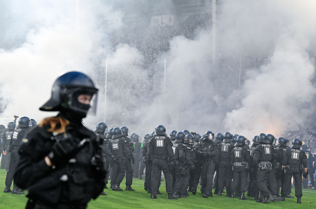 Police officers stand in front of the SV Waldhof Mannheim fan section as smoke caused by pyrotechnics lit by fans rise during the Germany Cup soccer match between SV Waldhof Mannheim and 1. FC Kaiserslautern, Friday, Aug. 21, 2026, in Mannheim, Germany. (Uwe Anspach/dpa via AP)