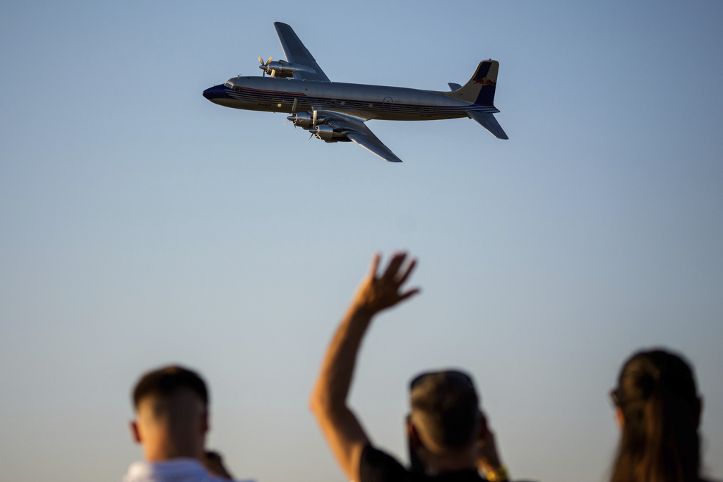 People wave as a Douglas DC-6B plane of the Flying Bulls Red Bull aerobatic team flies above the runway of the Aurel Vlaicu airport, on the first day of the Bucharest International Air Show, BIAS 2025 in Bucharest, Romania, Saturday, Aug. 30, 2025. (AP Photo/Andreea Alexandru)