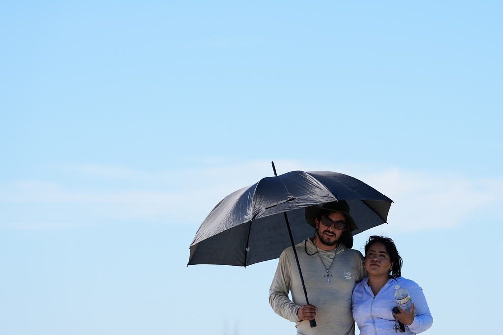 FILE - Juan Olmedo, left, and his wife Alejandra Delgado use an umbrella to shield from the sun while on a walk at Shoreline Park in Mountain View, Calif., March 16, 2026. (AP Photo/Godofredo A. Vásquez, File)