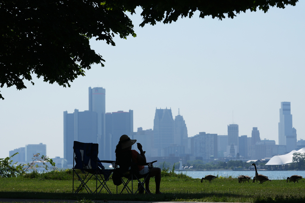 A woman sits in the shade to avoid the heat Monday, July 13, 2026, in Detroit. (AP Photo/Paul Sancya)