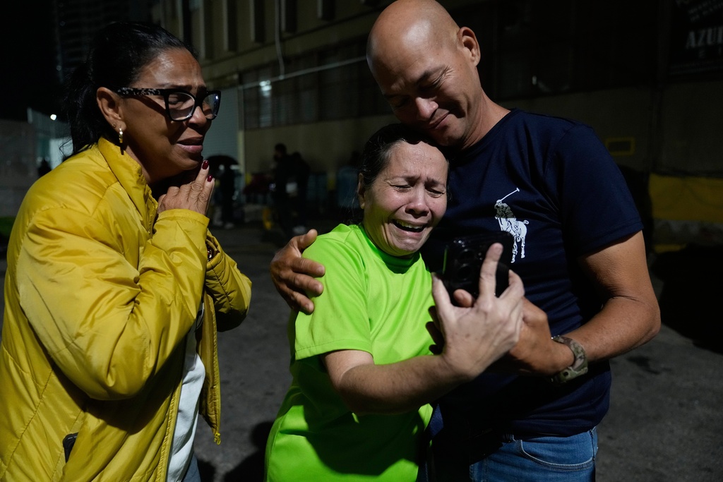 Morelba Delgado, en el centro, habla con un familiar por celular tras ser liberada del centro de detención Zona 7 de la Policía Nacional Bolivariana en Caracas, Venezuela, el sábado 14 de febrero de 2026. (Foto AP/Ariana Cubillos)