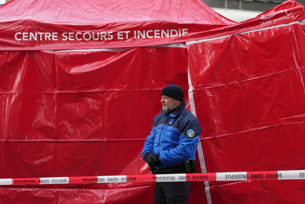 Police stands at an emergency tent beside the sealed off Le Constellation bar, where a devastating fire left dead and injured during the New Year's celebrations in Crans-Montana, Swiss Alps, Switzerland, Friday morning, Jan. 2, 2026. (AP Photo/ Antonio Calanni)