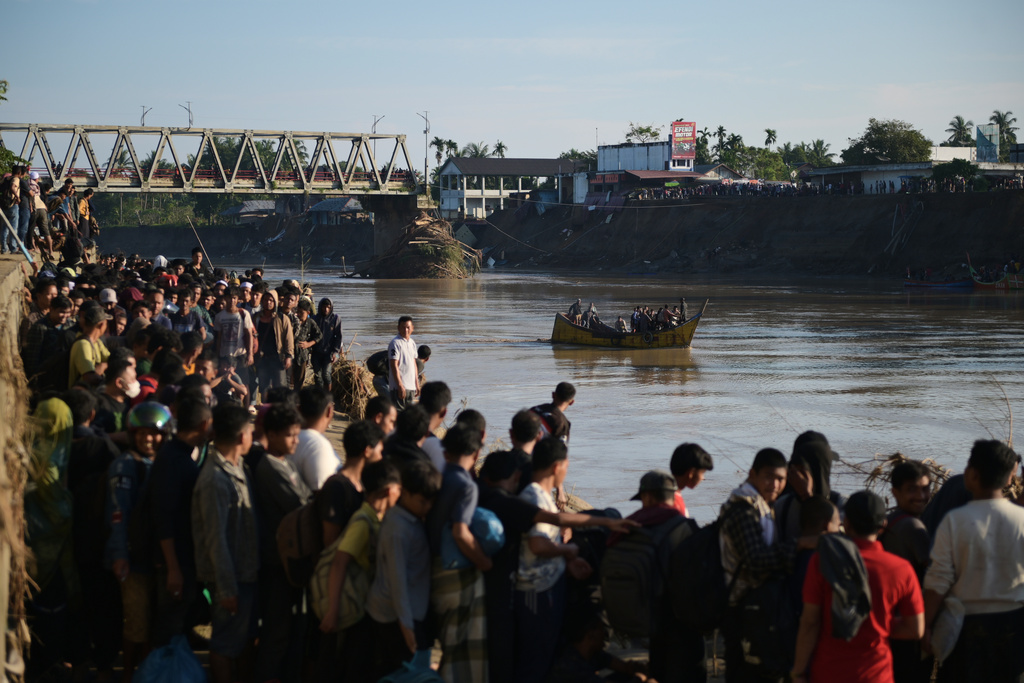 People wait for a boat to ride across a river after a bridge nearby collapsed during a flood in Bireun, Aceh province, Indonesia, Saturday, Nov. 29, 2025. (AP Photo/Reza Saifullah)