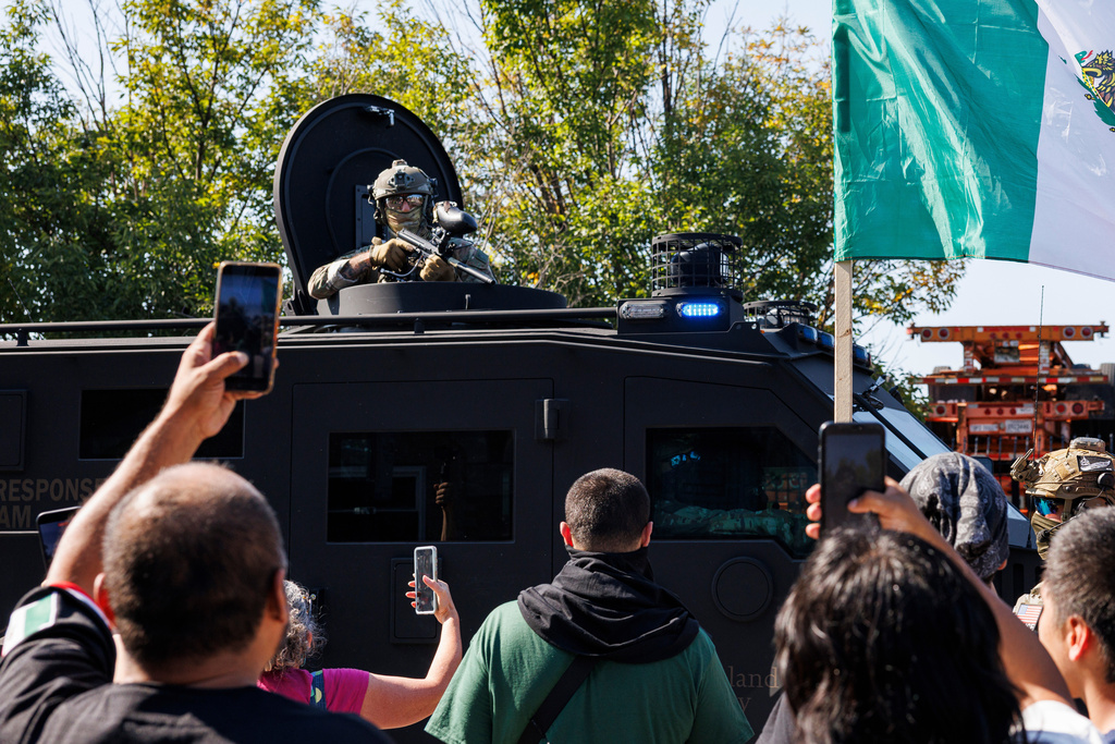 An ICE officer watches protestors as a Lenco BearCat vehicle drives to the scene in the Brighton Park neighborhood of Chicago, on Saturday, Oct. 4, 2025, after protesters learned that U.S. Border Patrol shot a woman Saturday morning on Chicago's Southwest Side. (Anthony Vazquez/Chicago Sun-Times via AP)