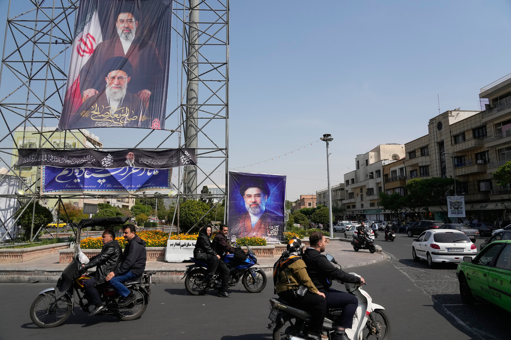 People drive their motorbikes past billboards showing the Iran's Supreme Leader Ayatollah Mojtaba Khamenei, top and right, and his father, the slain Supreme Leader Ayatollah Ali Khamenei, who was killed in U.S. and Israeli strikes on Feb. 28, in downtown Tehran, Iran, Thursday, April 16, 2026. (AP Photo/Vahid Salemi)