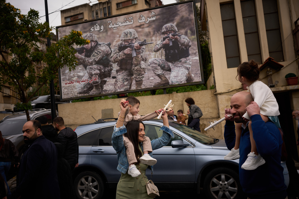 Catholic worshipers carry their children on their shoulders as they march in a procession during a Palm Sunday Mass in Beirut, Lebanon, Sunday, March 29, 2026. The poster in the background reads in Arabic: "Honor, sacrifice and loyalty". (AP Photo/Emilio Morenatti)