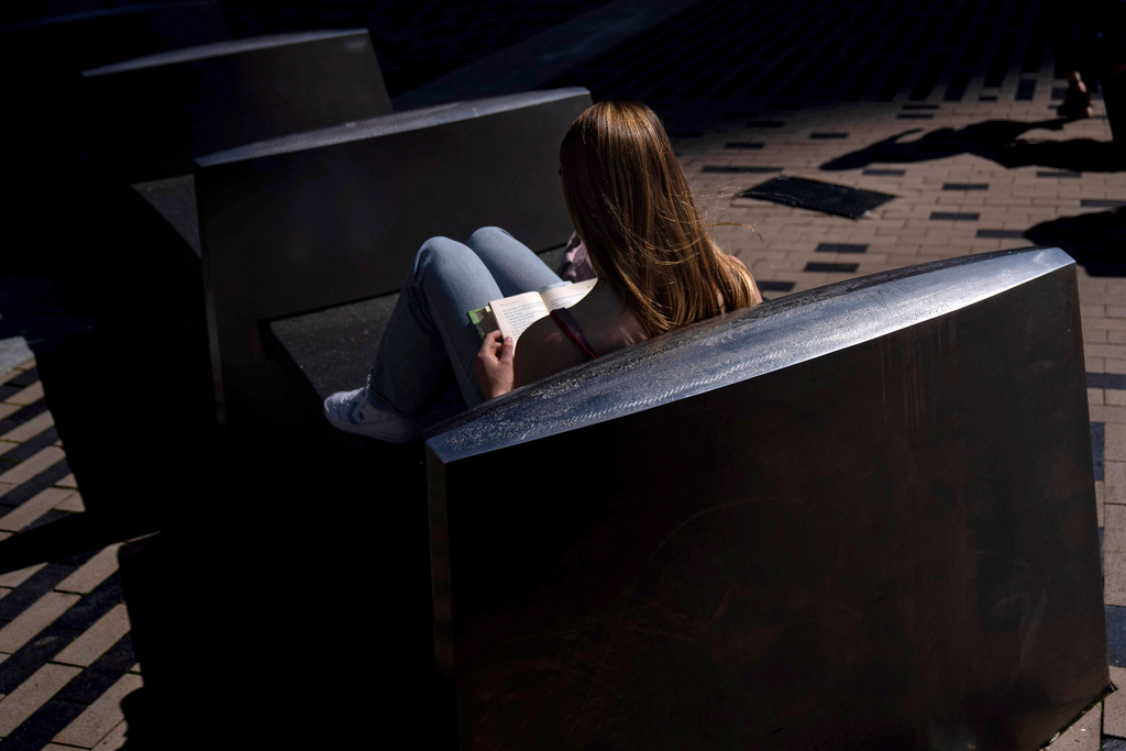 FILE - A woman reads a book in the afternoon sun on a bench outside South Station in Boston, on Friday, May 31, 2024. (AP Photo/David Goldman, File)