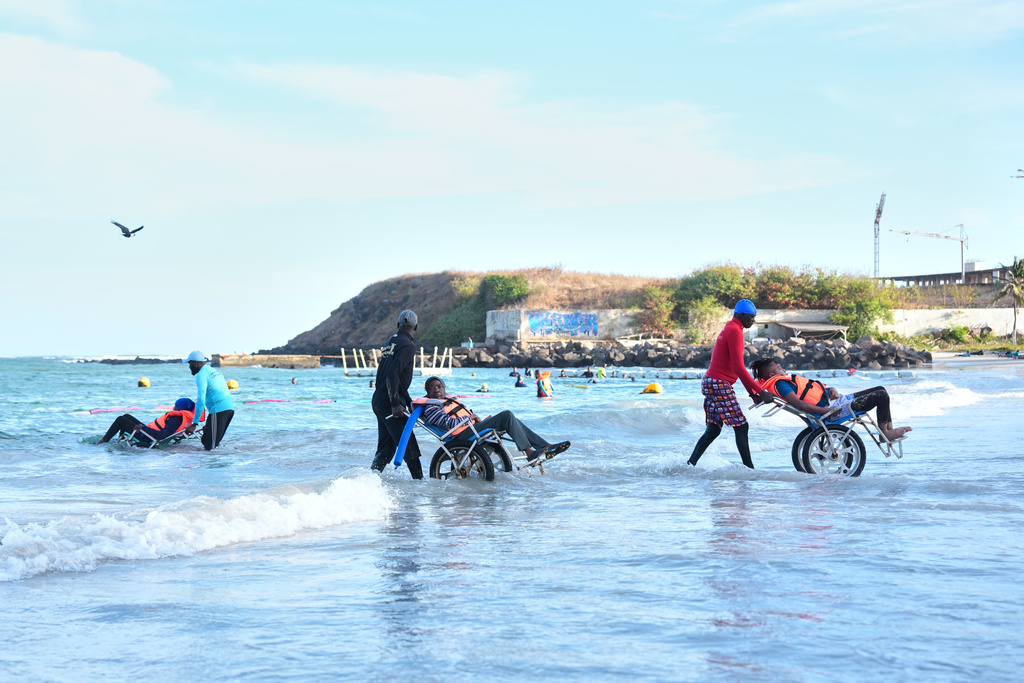 Instructors assist participants with limited mobility into the ocean for an aquatic therapy session in Dakar, Senegal, Saturday, Dec. 13, 2025. (AP Photo/Misper Apawu)