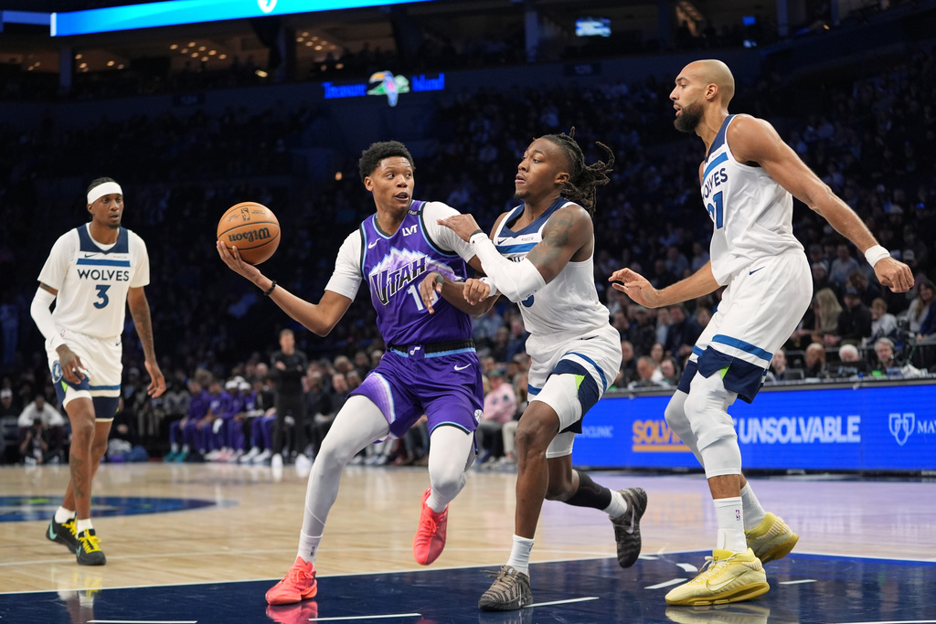 Utah Jazz guard Ace Bailey (19), second left, works toward the basket as Minnesota Timberwolves guard Ayo Dosunmu (13), second right, and center Rudy Gobert (27), right, defend during the first half of an NBA basketball game, Wednesday, March 18, 2026, in Minneapolis. (AP Photo/Abbie Parr)