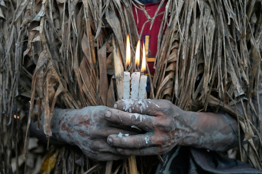 A Catholic devotee covered in mud and dried banana leaves holds candles during the mud people festival on the feast day of Saint John the Baptist at Bibiclat, Nueva Ecija province, northern Philippines on Wednesday, June 24, 2026. (AP Photo/Aaron Favila)