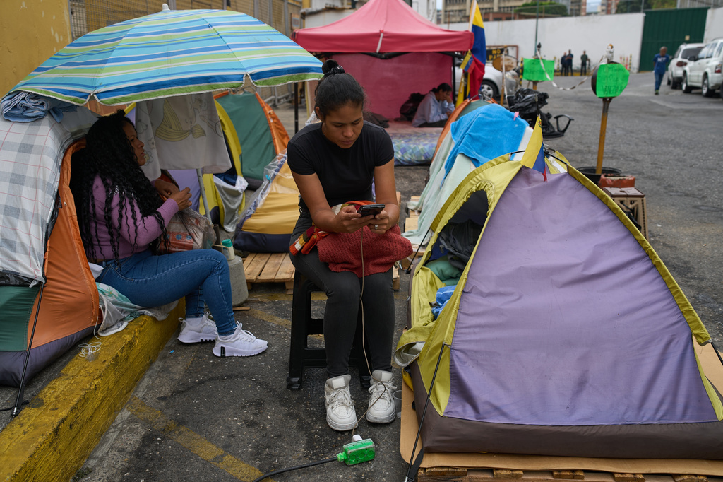 Sandra Rosales uses her phone while camping outside the gates of a Bolivarian National Police detention center where her husband, Dionnys Quintero, is being held on political grounds in Caracas, Venezuela, Thursday, March 12, 2026. (AP Photo/Ariana Cubillos)