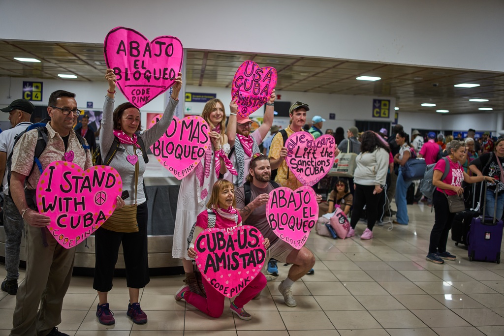 Activists from CODEPINK, including co-founder Medea Benjamin, kneeling center, and others hold signs as part of the "Nuestra America," or Our America Convoy after landing at the airport in Havana, Cuba, Friday, March 20, 2026. (AP Photo/Ramon Espinosa)