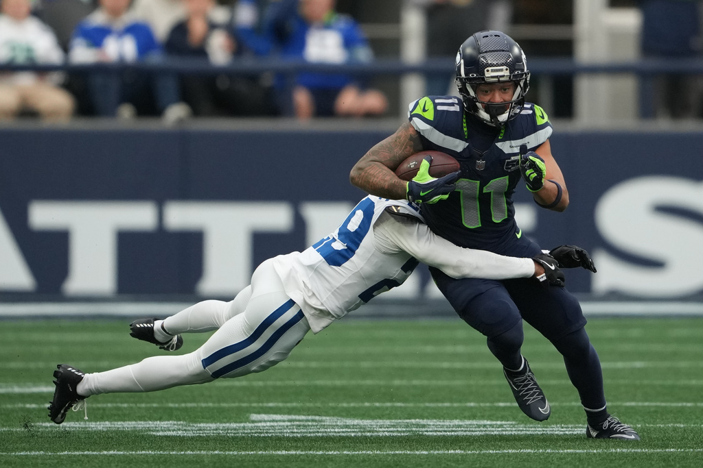 Jaxon Smith-Njigba (11), wide receiver de los Seahawks de Seattle, es derribado por Mekhi Blackmon (29), de los Colts de Indianápolis, durante la segunda mitad del partido de la NFL, el domingo 14 de diciembre de 2025, en Seattle. (AP Foto/Lindsey Wasson)