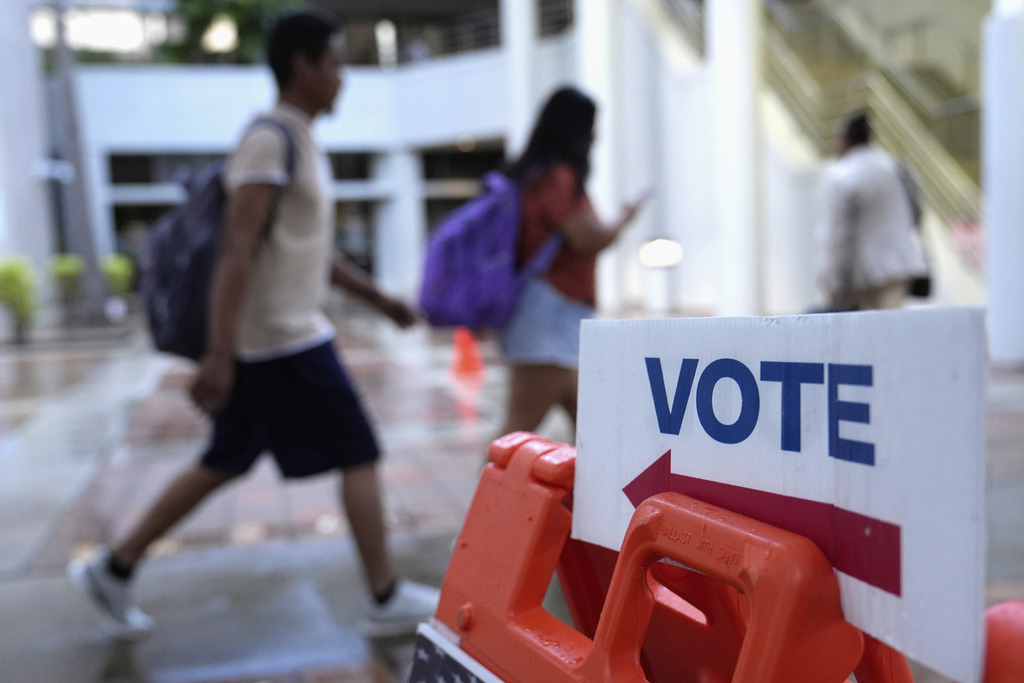 FILE - People walk past a "vote" sign on the first day of early voting in the general election in Miami, on Oct. 21, 2024. (AP Photo/Lynne Sladky, File)