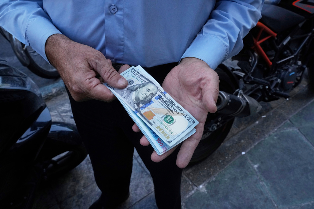 FILE — A street money exchanger poses for a photo without showing his face as he holds U.S. and Iranian banknotes at Ferdowsi square, Tehran's go-to venue for foreign currency exchange, in downtown Tehran, Iran, Aug. 28, 2025. (AP Photo/Vahid Salemi, File)