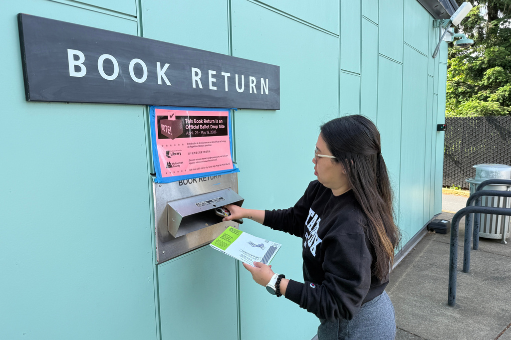 A voter drops off their ballot at a library in Portland, Ore. serving as a ballot dropbox site as Oregon held primary elections on May 19, 2026. (AP Photo/Claire Rush)