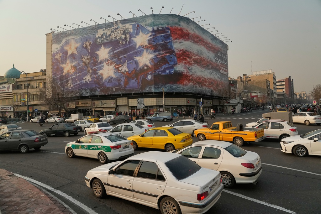 Vehicles drive past a billboard depicting a damaged U.S. aircraft carrier with disabled fighter jets on its deck and a sign reading in Farsi and English, "If you sow the wind, you'll reap the whirlwind," at Enqelab-e-Eslami (Islamic Revolution) Square in Tehran, Iran, Sunday, Jan. 25, 2026. (AP Photo/Vahid Salemi)