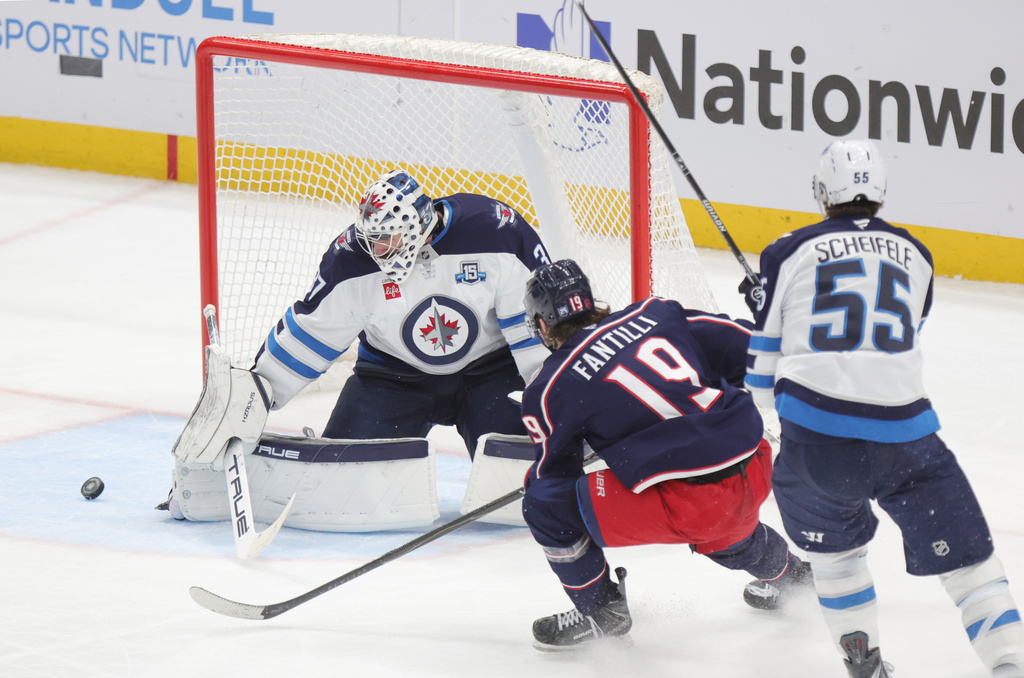 Winnipeg Jets goalie Connor Hellebuyck, left, stops a shot in front of Columbus Blue Jackets forward Adam Fantilli and Jets forward Mark Scheifele during the third period of an NHL hockey game in Columbus, Ohio, Saturday, April 4, 2026. (AP Photo/Paul Vernon)