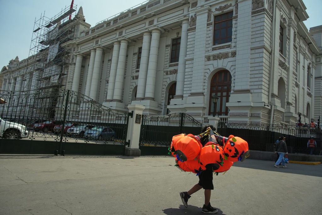 A vendor carries Halloween-themed pumpkin piñatas past Congress in Lima, Peru, Friday, Oct. 10, 2025, the day lawmakers voted to remove President Dina Boluarte from office. (AP Photo/Guadalupe Pardo)
