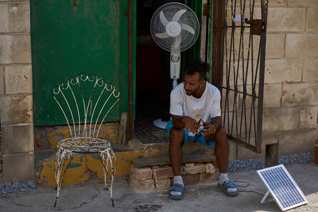 A man charges his fan's battery at his doorway using a small solar panel set up on the street during a blackout in Havana, Cuba, Friday, Sept. 18, 2026. (AP Photo/Ramon Espinosa)