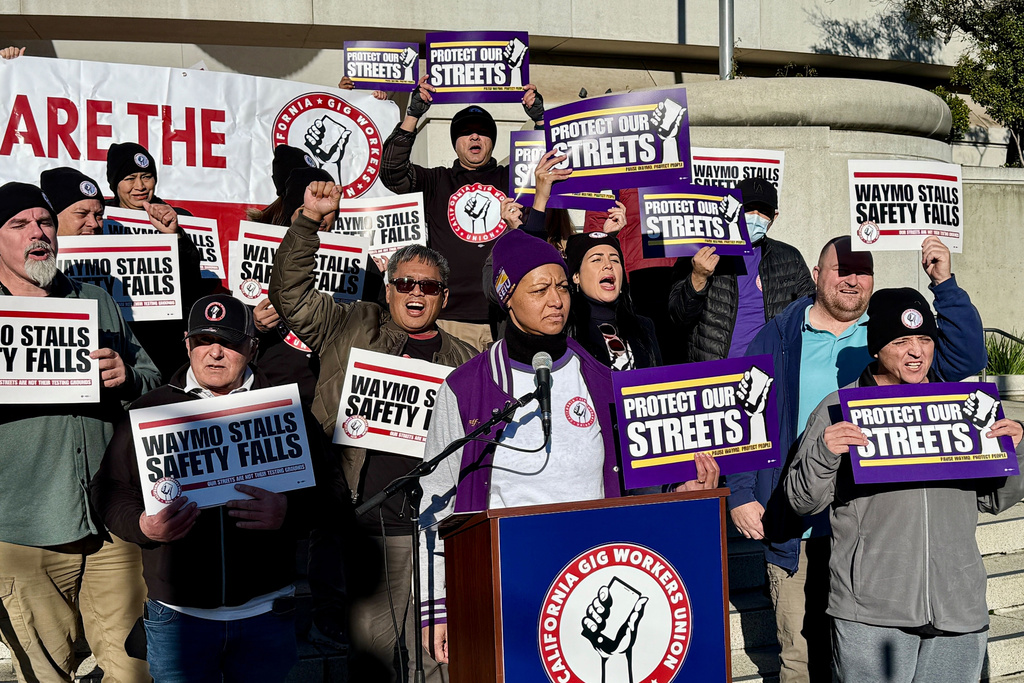 Demonstrators holds signs during a protest by Uber and Lyft drivers asking state regulators to take self-driving taxis off the streets due to safety concerns at the California Public Utilities Commission headquarters Friday, Jan. 9, 2026, in San Francisco. (AP Photo/Haven Daley)