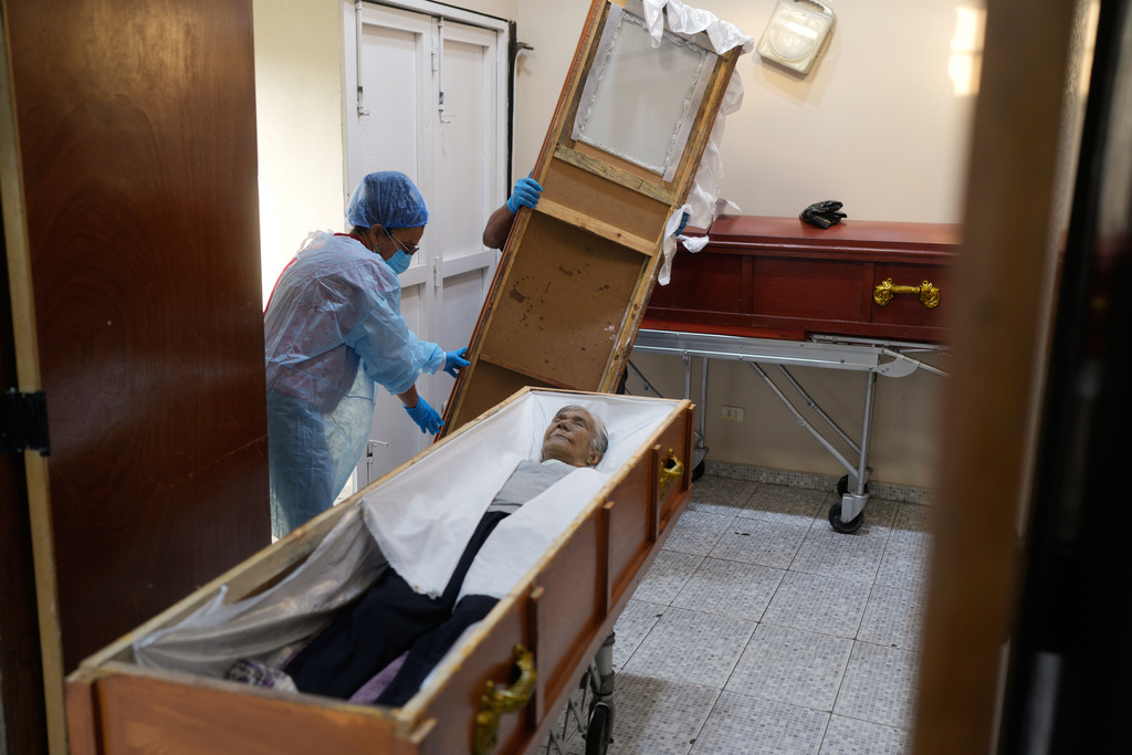 Funeral workers prepare the body of Rosa Elena Gonzalez, 80, who died after her apartment was hit during a U.S. strike to capture President Nicolas Maduro, in Catia La Mar, Venezuela, Sunday, Jan. 4, 2026. (AP Photo/Matias Delacroix)