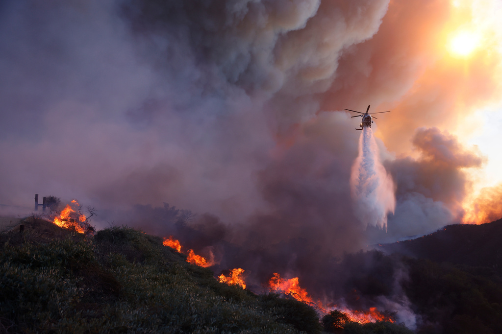FILE - Water is dropped by helicopter on the advancing Palisades Fire in the Pacific Palisades neighborhood of Los Angeles, Jan. 7, 2025. (AP Photo/Etienne Laurent, File)