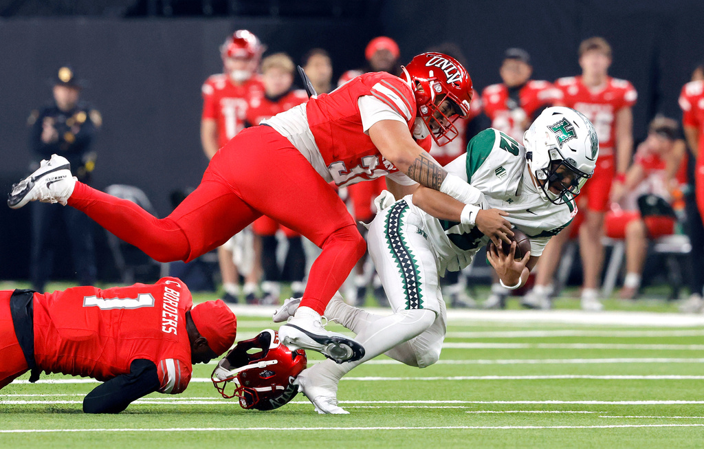 Hawaii quarterback Micah Alejado (12) is sacked by UNLV defensive end Kenji Scanlan (32) during the first half of an NCAA football game Friday, Nov. 21, 2025, in Las Vegas. UNLV linebacker Chief Borders (1) loses his helmet at left. (Steve Marcus/Las Vegas Sun via AP)