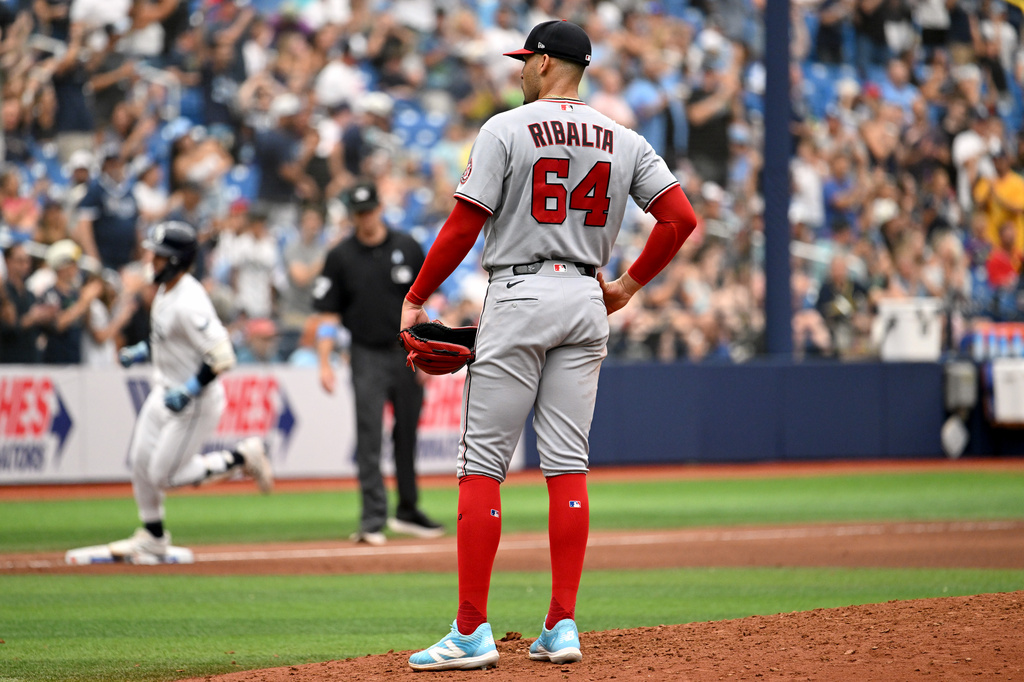 Washington Nationals pitcher Orlando Ribalta (64) looks away as Tampa Bay Rays' Jonny DeLuca, back left, rounds the bases after hitting a two-run home run during the seventh inning of a baseball game Sunday, June 21, 2026, in St. Petersburg, Fla. (AP Photo/Jason Behnken)
