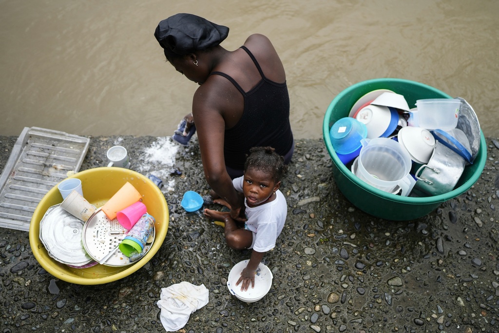 FILE - A mother and her baby wash dishes in the Atrato River, in El Arenal, Colombia, Sept. 26, 2024. (AP Photo/Ivan Valencia, File)