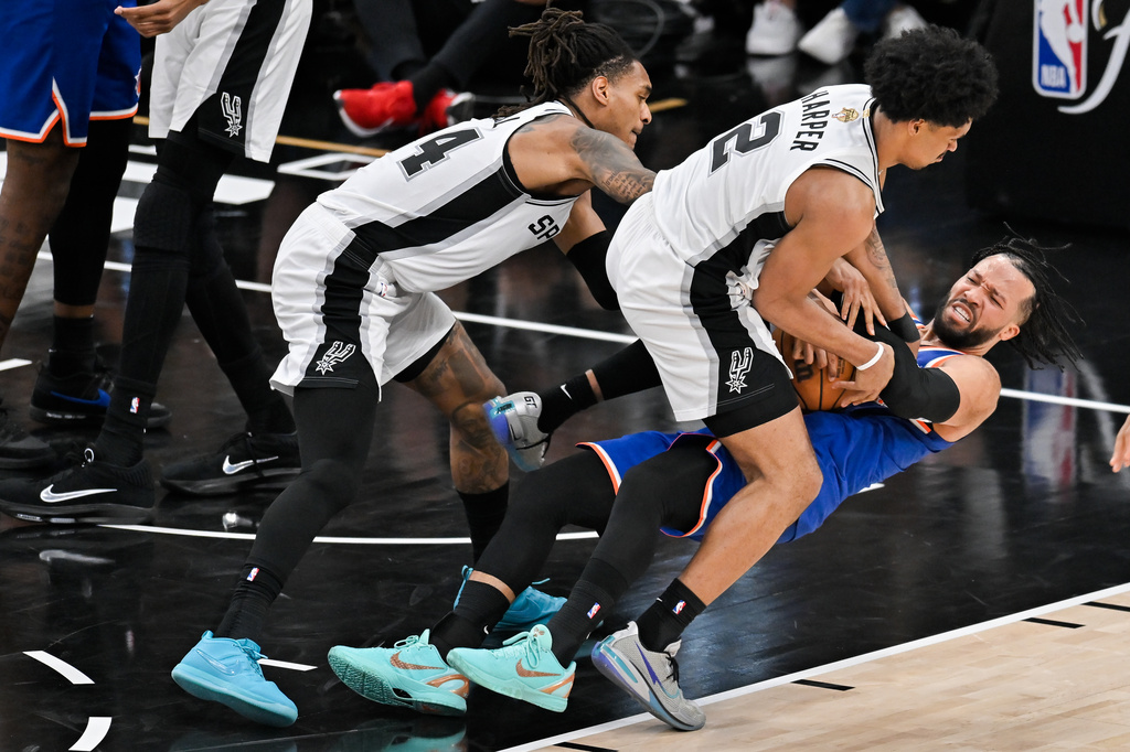 New York Knicks guard Jalen Brunson falls as he pressured by San Antonio Spurs guard Dylan Harper (2) and guard Devin Vassell during the second half of Game 5 of the NBA Finals basketball series, Saturday, June 13, 2026, in San Antonio. (AP Photo/Darren Abate)