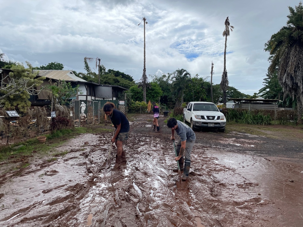 Madison Nahooikaika in the background looking for items lost during the flooding, while in the foreground, her boyfriend, Nuutea Vanbastolaer, and a neighbor shovel out mud, in Haleiwa, Hawaii, on Saturday, March 21, 2026. (San Francisco Chronicle via AP)