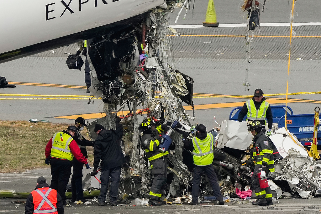 Port Authority fire fighters and aircraft maintenance crews cut away debris from the wreckage of an Air Canada Express jet, Wednesday, March 25, 2026, just off the runway where it had collided with a Port Authority fire truck Sunday night at LaGuardia Airport in New York. (AP Photo/Yuki Iwamura)